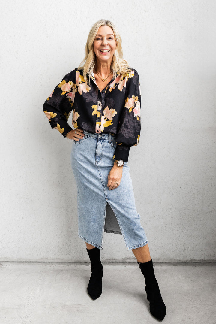 Woman wearing a floral blouse, denim skirt, and black boots against a plain background