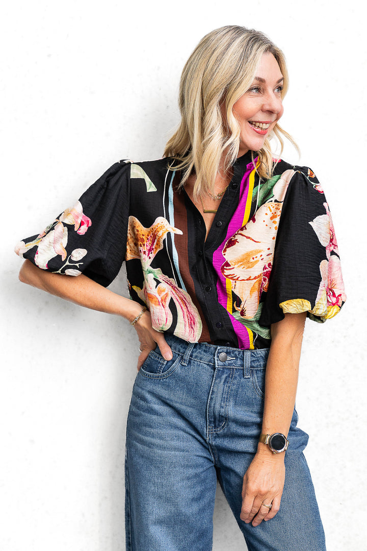 Woman wearing a floral blouse with a colorful scarf and jeans against a white background